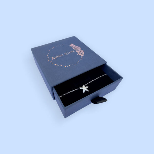 Inspiring silver anklet with a starfish charm, presented in a blue jewellery box with Anklet Allure written on the top in rose gold.