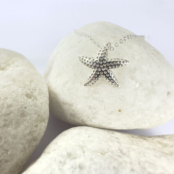 Close up of the charm of a starfish on a silver anklet.