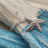 Starfish charm on a sterling silver anklet on a blue and white beachy looking wood.
