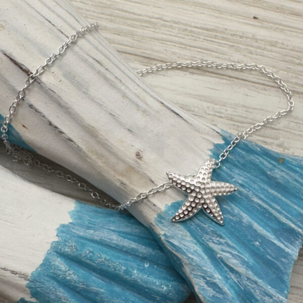 Beach chic sterling silver anklet with a starfish charm with a dotted look on the surface of the starfish on a blue and white washed wood.