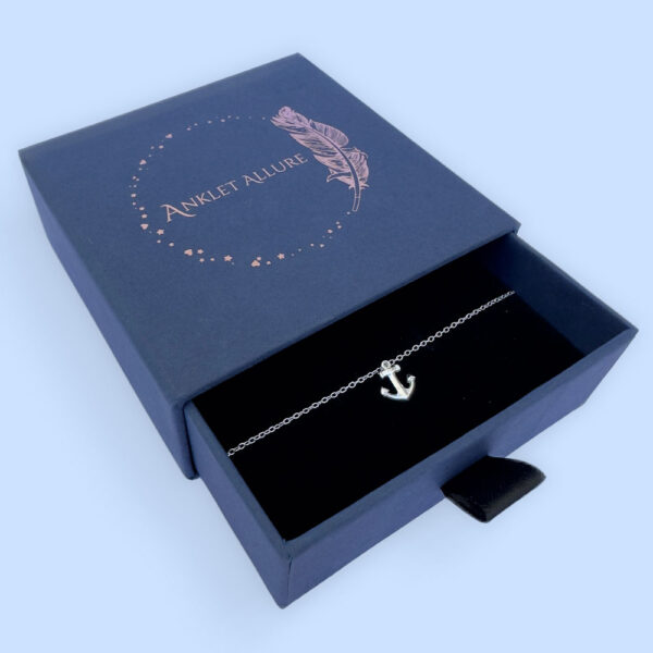 Grounding anklet with a silver anchor charm, presented in a blue jewellery box with Anklet Allure written on the top in rose gold.