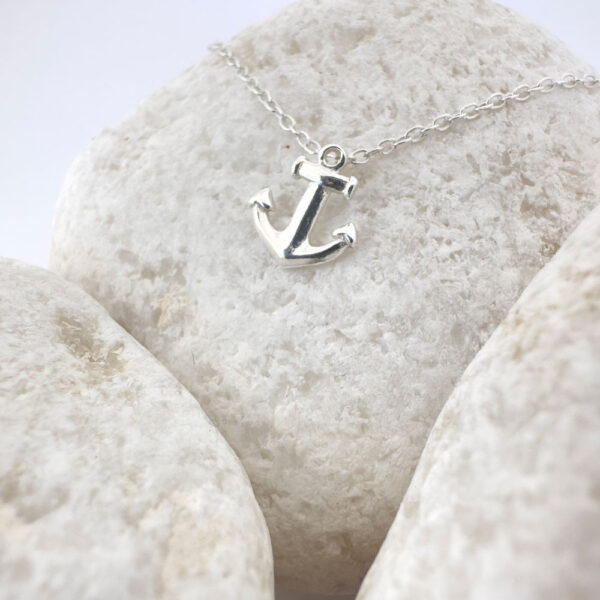 Close up of a silver anchor charm on a white rock.