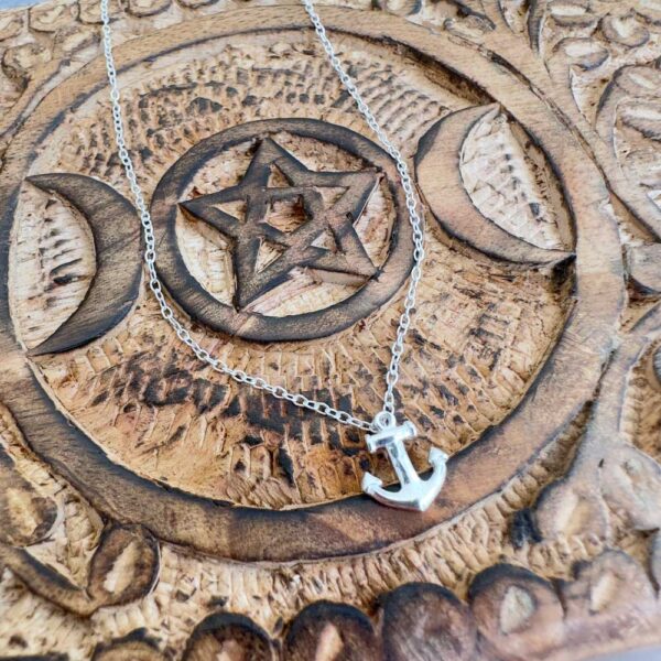 Silver anklet with anchor charm displayed on patterned wood.