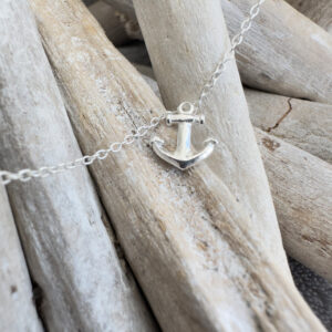A silver anklet with a silver anchor charm displayed on white-washed sticks.
