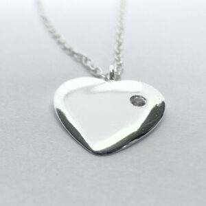 Close up of a heart charm with a dainty gemstone on a silver ankle bracelet.