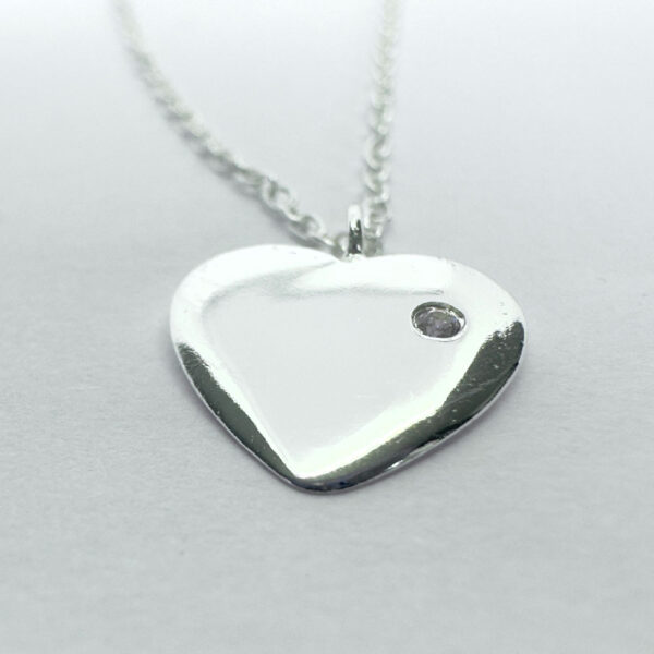 Close up of a heart charm with a dainty gemstone on a silver ankle bracelet.