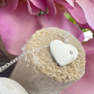 Solid sterling silver anklet with a heart charm with a dainty white gem displayed on the end of a stick with purple petals in the top right background.