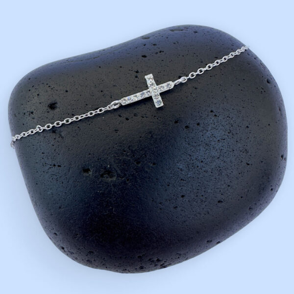 Silver anklet with a shiny gem encrusted cross within the chain.
