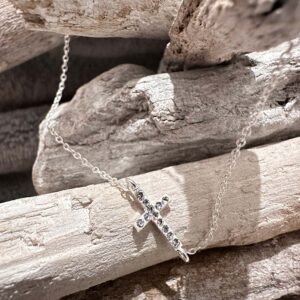 Silver anklet with a cross charm along it with twelve gems on top presented on some white-washed sticks.