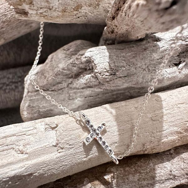 Silver anklet with a cross charm along it with twelve gems on top presented on some white-washed sticks.