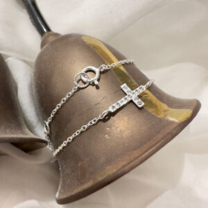 SIlver cross anklet with cubic zirconia gems along the cross and wrapped around an antique gold bell.