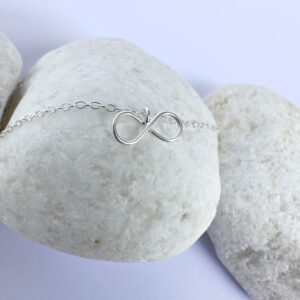 Close up of an eye catching silver ankle bracelet with a dainty infinity charm.