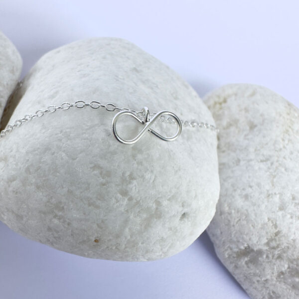 Close up of an eye catching silver ankle bracelet with a dainty infinity charm.