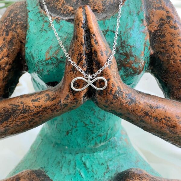 Silver infinity charm anklet displayed on a green and brown yoga woman with hands in prayer.