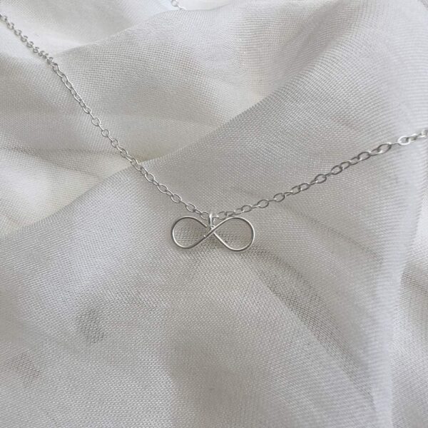 Dainty infinity charm on a silver ankle bracelet.
