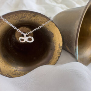 Silver infinity anklet displayed on a set of brass bells, laid on their side on a white fabric.