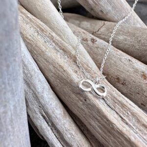 Infinity sterling silver charm on anklet sitting on a wooden stick.