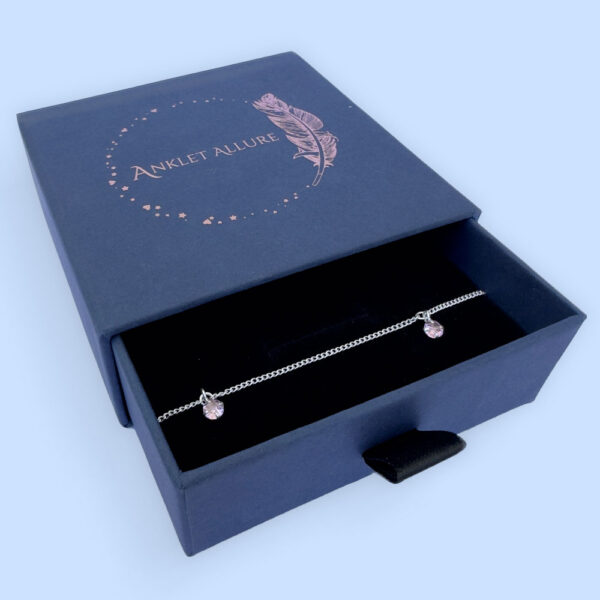 Sterling silver anklet with three pink gemstones, presented in a blue jewellery box with Anklet Allure written on the top in rose gold.