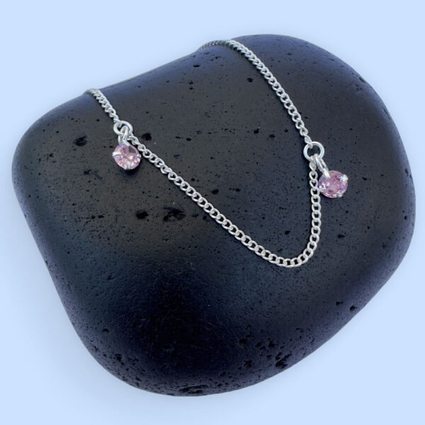 Stunning silver anklet with two gemstones displayed on a black stone with a blue background.