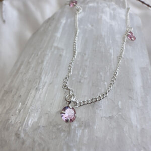 Passionate pink coloured gemstones positioned around a sterling silver ankle bracelet, on top of a white crystal.