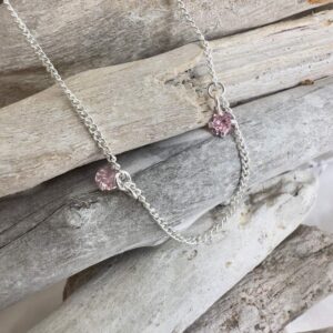 Silver anklet with pink cubic zirconia gems hanging from it, displayed on wooden sticks.