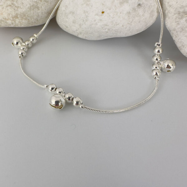 Silver anklet with large round charms with two smaller round charms either side, presented on white rocks.