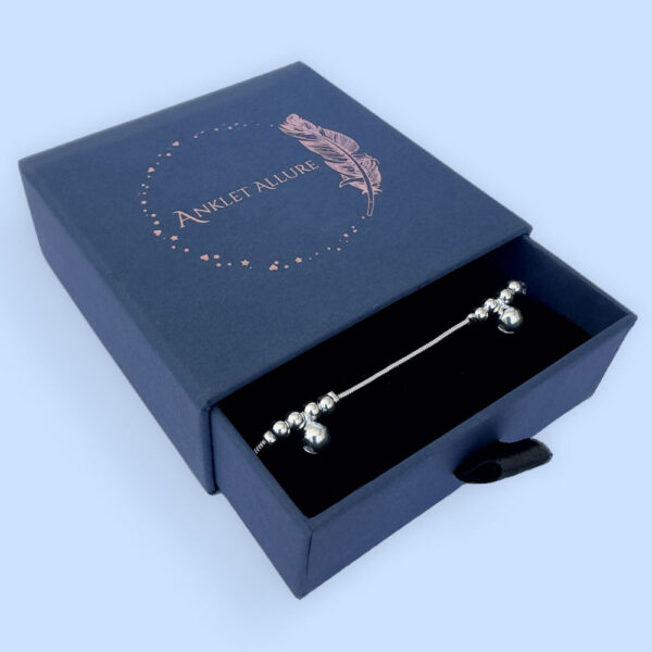 Silver anklet with large round charms with two smaller round charms either side, presented in a blue jewellery box.