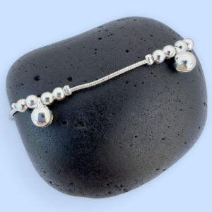 Silver anklet with large round charms with two smaller round charms either side, presented on a black rock.