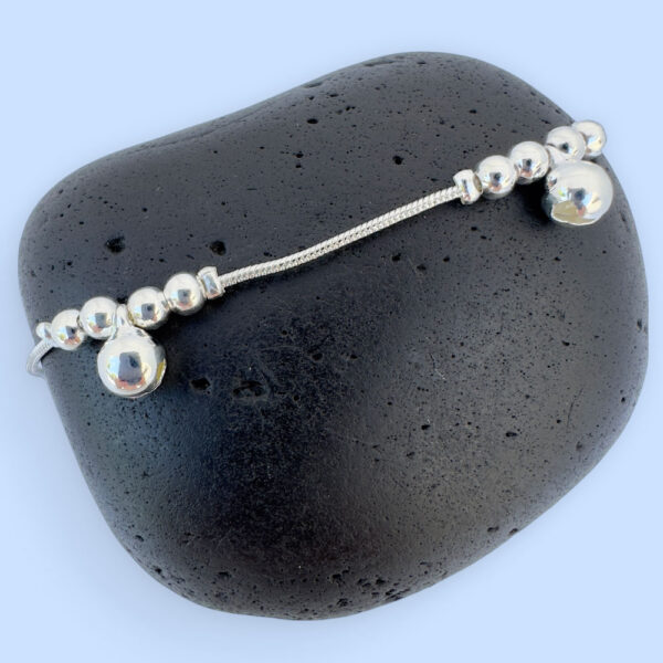 Silver anklet with large round charms with two smaller round charms either side, presented on a black rock.
