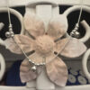 Silver anklet with three groups of four balls and a bell, hanging off a pink and white metal flower background.