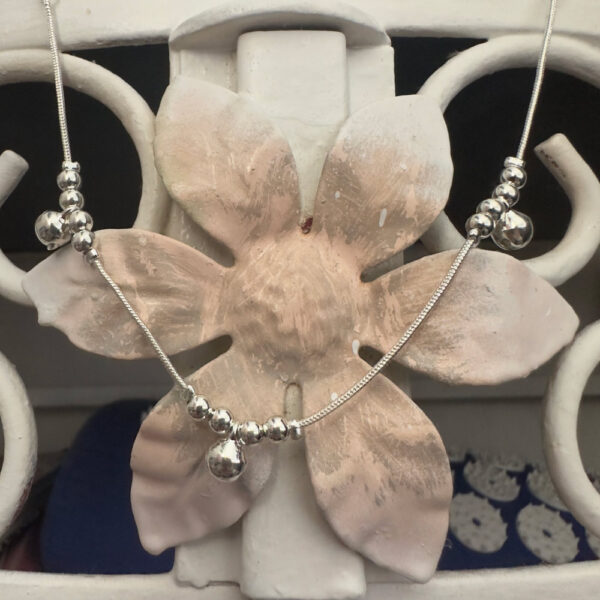 Silver anklet with three groups of four balls and a bell, hanging off a pink and white metal flower background.
