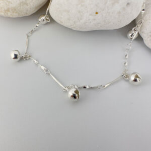 Jingly silver anklet with a stiff twisted chain and three bells equally spaced around, presented on white rocks.