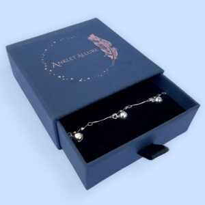 Silver anklet with a stiff twisted chain and three bells equally spaced around, presented in a dark blue Anklet Allure gift box.