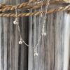 Silver anklet with jingling balls on a silver chain designed to look twisted, on a black and white painted wood background with rope around the top.