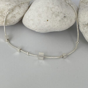 Ankle bracelet in silver with different sized square charms on white rocks.