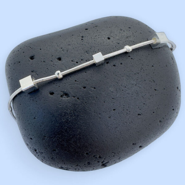 Ankle bracelet in silver with different sized square charms on a black rock.
