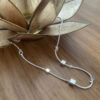 Silver ankle bracelet with five square box charms on a wooden table draped over a gold lotus shaped candle holder.