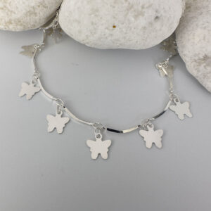 Stiff silver ankle chain with solid butterfly charms on white rocks.
