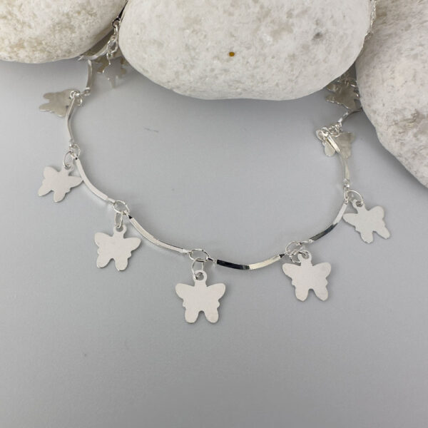 Stiff silver ankle chain with solid butterfly charms on white rocks.