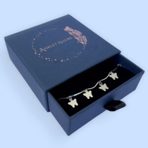 Stiff silver ankle chain with solid butterfly charms in a blue jewellery box.