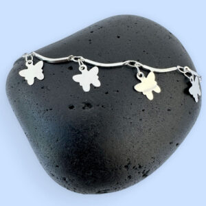 Stiff silver ankle chain with solid butterfly charms on a black rock.