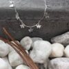 Silver anklet with butterfly charms spaced equally around the simple chain draped over a black concrete step with white stones in the foreground.
