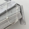 Double chain silver anklet with a heart between two silver balls, repeated three times around the chain, hanging from white washed wood