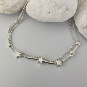 Stunning double chain silver ankle bracelet with three star charms and two small frosted ball charms either side on white rocks.