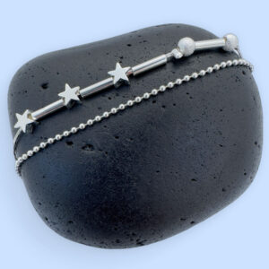 Double chain silver anklet with three star charms and two small frosted ball charms on a black rock.