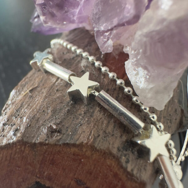 Close up of double chain anklet with star charms, draped on wood with purple crystal in the background.