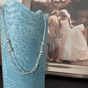 Silver anklet with a mix of small silver balls and silver stars, hanging over a blue candle with a couple kissing on their wedding day in the background.
