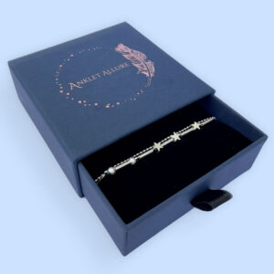 Double chain silver anklet with three star charms and two small frosted ball charms in a blue jewellery box.