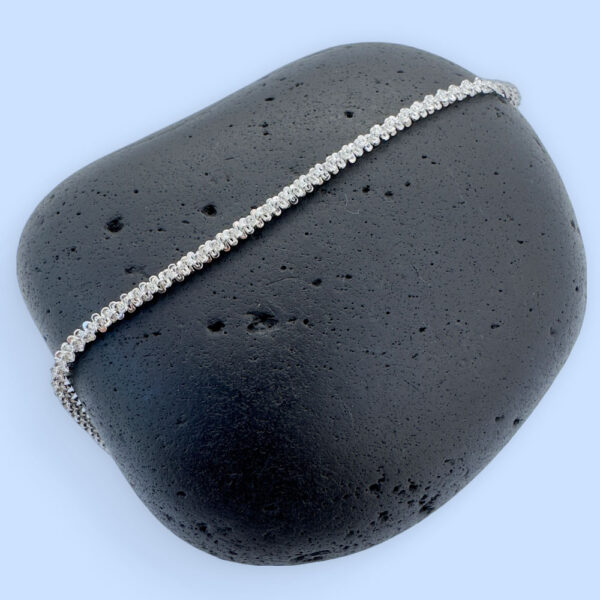 A simple sparkly ankle bracelet on a black rock.