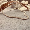 A simple silver anklet that sparkles, presented on a charcoal coloured rock hanging over a brown leaf.